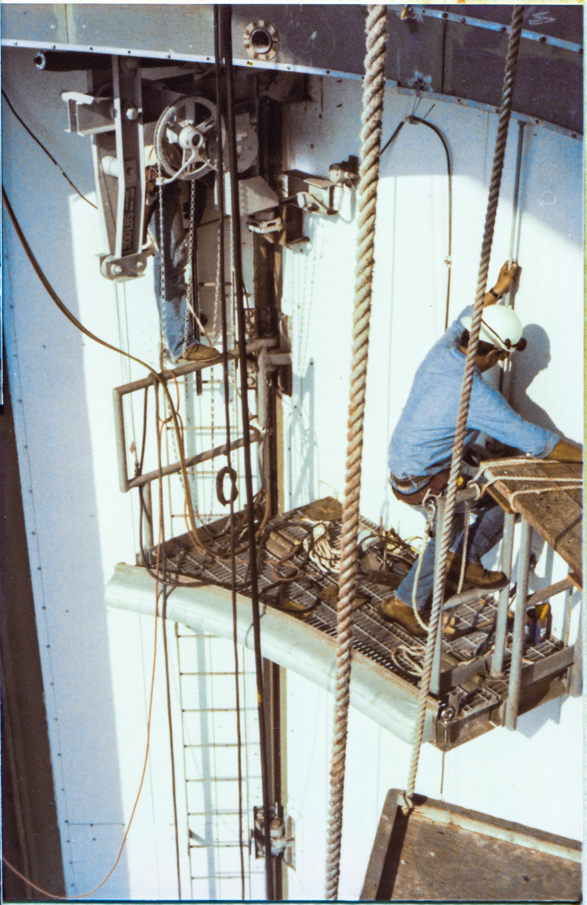 Image 063. Union Ironworkers from Local 808, working for Ivey Steel at Space Shuttle Launch Complex 39-B, Kennedy Space Center, Florida, have lashed scaffoldboards between the upper set of Torque Tube Access Platforms fixed and removable handrails, providing complete (although scary as hell, too) access across both of the Payload Changeout Room Main Doors, and are using the Platforms to give them access to the Hoists associated with them, which are being installed as you're seeing it. This work is proceeding just beneath the ”ledge” of the Antenna Access Platform at elevation 198'-7½”, nearly 60 feet above the far edge of the RSS Main Floor steel in the Orbiter Mold Line area, which itself is another 80 feet above the concrete of the pad deck. Photo by James MacLaren.